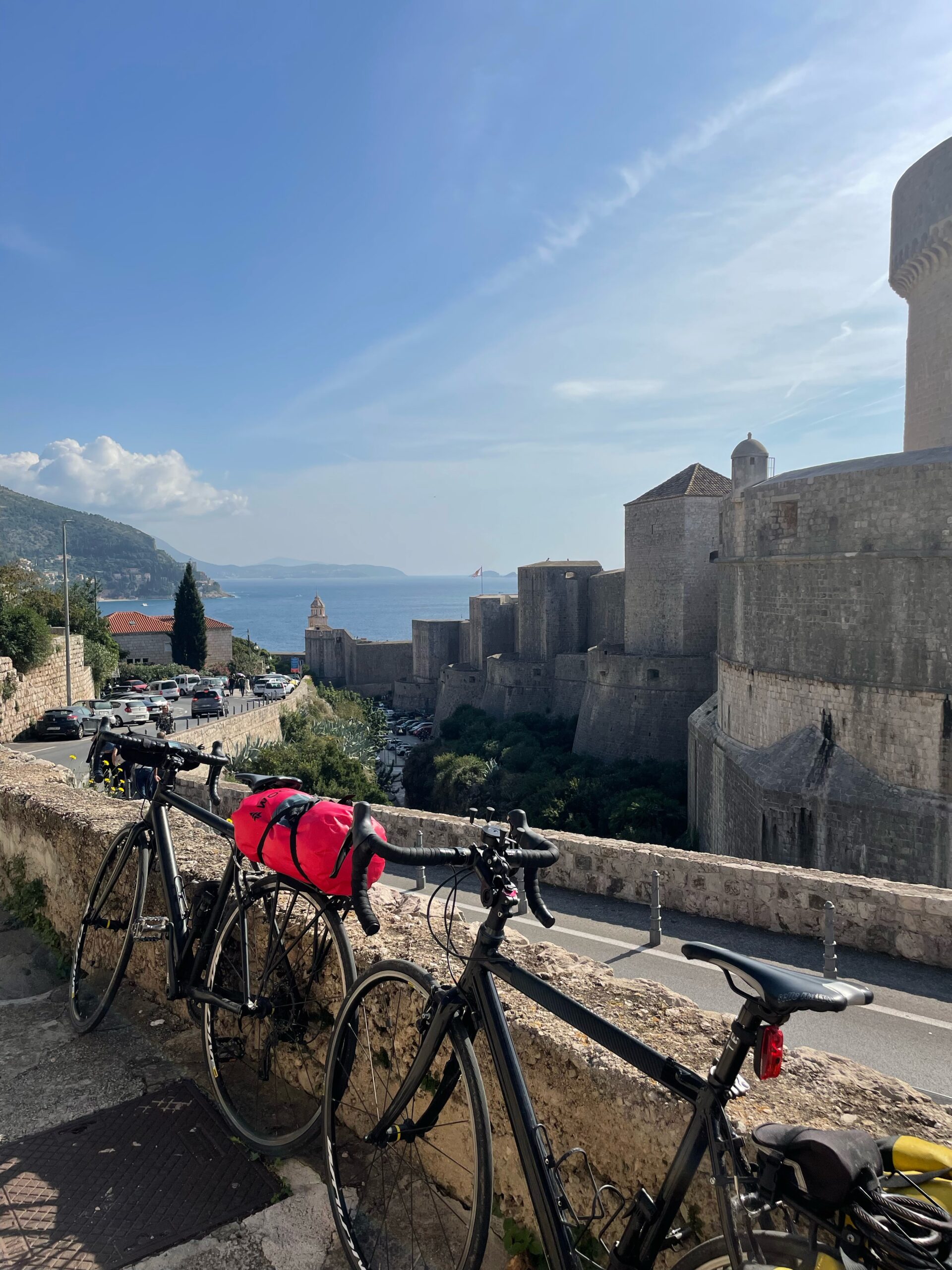 Two bicycles parked beside a stone wall, with a view of the Adriatic Sea and Dubrovnik's historic buildings in the background, under a clear blue sky - the final stop of our Croatia by bike journey.